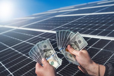 hand of a young man holding dollars to pay for the installation of new solar panels. Concept of green electricity. saving electricity