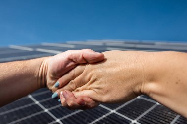 Handshake in front of solar energy photovoltaic panels outdoors. concept of agreement before installing solar panels