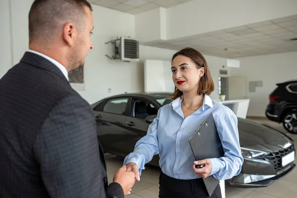 young pretty client shaking hands with man sales dealer in modern car showroom, success deal. concept of purchase vehicle