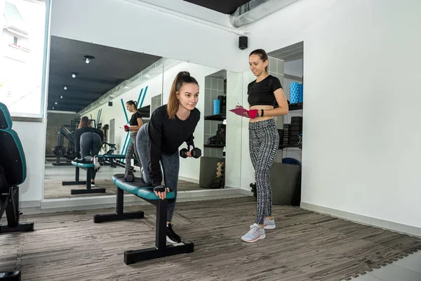 young sports trainer with a good figure trains a young client who came to the gym to improve her figure. The concept of being overweight in a woman. training with a trainer