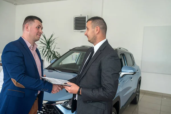 serious man buys an expensive car from a representative of a car dealership and shakes his hand as a sign of agreement. buying and selling cars. car dealership