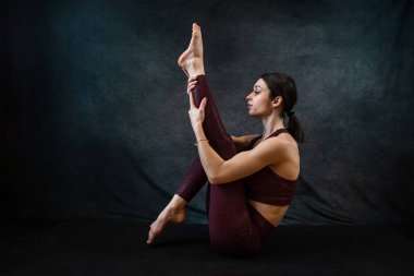 Spor kıyafetli, beyaz, çekici bir kadın stüdyonun koyu siyah arka planında yoga yapıyor. Kuvvet ve motivasyon