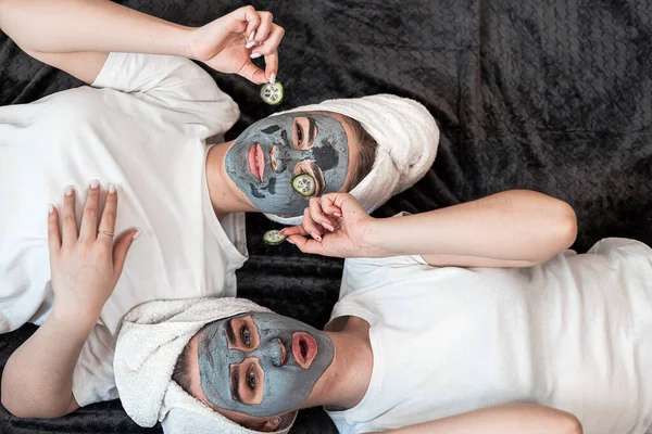 Two female friends lying on the floor together with facial masks and slice cucumbers for the freshness of the skin around the eyes. Skincare or natural care, beauty treatment