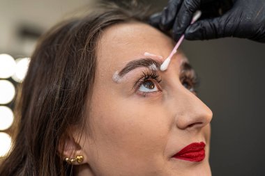 Bir kaş sanatçısı güzel bir müşterinin kaşlarını kaplıyor. Kaş boyama kaplaması.