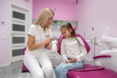 children's dentist conducts a consultation for a little girl in a dental chair. children's dentistry. the doctor talks about the importance of oral care