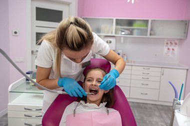 Lateks eldivenli genç beyaz dişçi dişlerinin durumunu kontrol ediyor. Dişçi koltuğundaki kız. sağlık