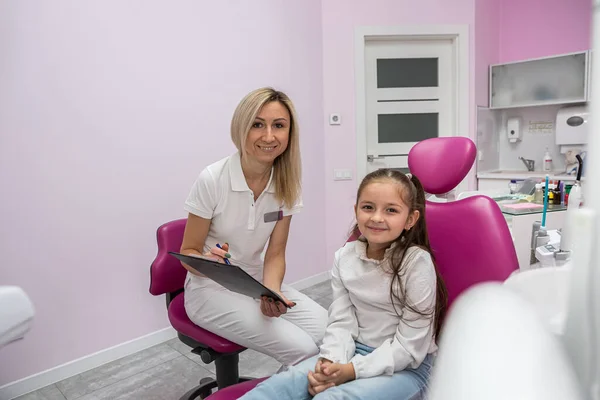 happy female dentist is interviewing a little girl patient in the office of a children\'s dental clinic. Dentistry technology. technology and healthcare concept. children\'s dentistry