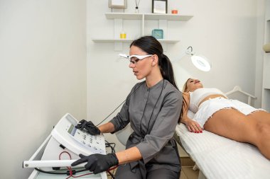 Kadın bir doktor elektroepilasyonla kozmetoloji prosedürüne hazırlanıyor. Güzellik konsepti Modern bir aletle derideki istenmeyen kılların çıkarılması.