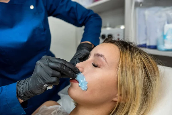 master applying cosmetics gel wax upper lip before hair removal procedure in clinic. Cosmetology procedure with sugar and wax. Sugaring. Depilation