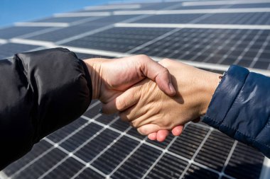 Two people shaking hands against a solar panel after signing a renewable energy deal. concept of solar panels