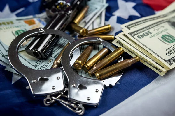 seized money and a gun with handcuffs and casings against the background of an American flag lying carelessly .vertical shot crime and punishment.
