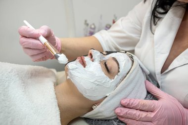 Kadın hastasına kaplıca salonunda beyaz kozmetik maske takan kozmetik uzmanının yakın çekimi. Kırışıklık önleyici kozmetik prosedür kavramı