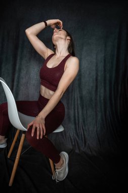 Atletik esmer genç kadın stüdyo çekiminde sandalyede oturan külüstür sutyen giyiyor. Sportif yaşam tarzı