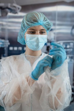 Genç bayan doktor ya da asistan cerrah ameliyathanede mavi koruyucu eldiven takıyor. Tıp ve sağlık hizmetleri kavramı