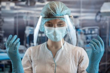 Genç bayan doktor ya da asistan cerrah ameliyathanede mavi koruyucu eldiven takıyor. Tıp ve sağlık hizmetleri kavramı