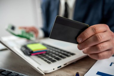 Takım elbiseli adam internetten alışveriş yapıyor ve evde ya da ofiste dizüstü bilgisayarla ödeme yapıyor.