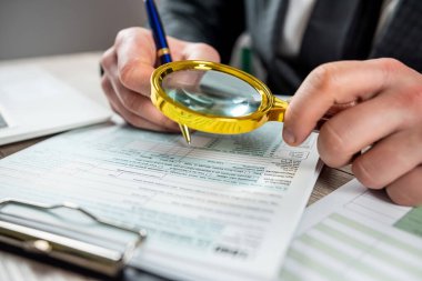 İş adamı ofisinde büyüteç kullanarak 1040 boş vergi formuna bakıyor. Muhasebe kavramı, vergi zamanı