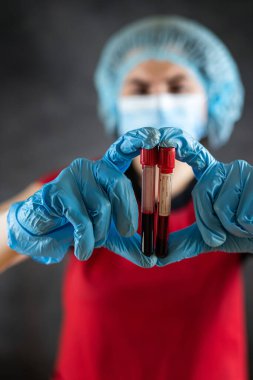 Kırmızı üniformalı laboratuvar asistanı, siyah üzerinde izole edilmiş test tüpündeki kan örneklerine bakıyor. Covid19 pozitif test sonucu. Tıbbi tanı 