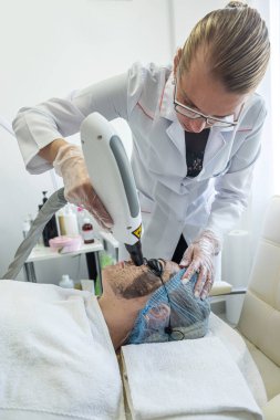 Tıbbi maske ve lastik eldiven takan profesyonel bir dermatolog müşterinin yüzüne maske takar. Güzellik salonlarında profesyonel yardım kavramı. Kozmetoloji.