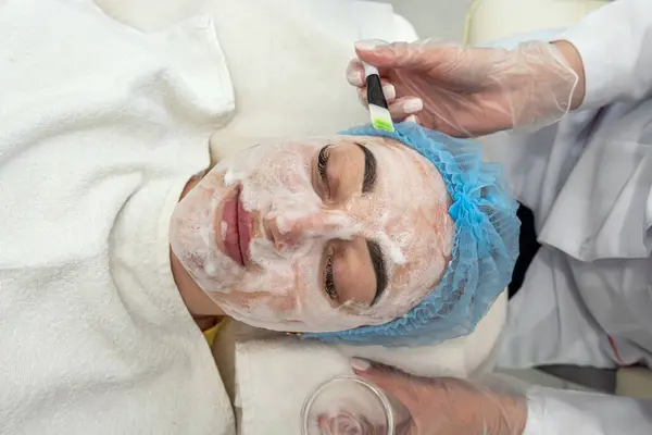 Cosmetologo Applica Una Maschera Nera Sul Viso Una Bella Donna — Foto Stock