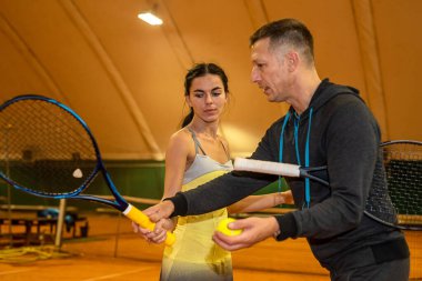 Erkek tenis koçu bir bayan müşteriye sahada nasıl servis yapılacağını gösteriyor. Spor. tenis dersleri