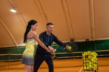 Genç erkek tenisçi bir kadına kortta tenis oynamayı öğretir. Tenis kortunda ellerinde raket olan bir çift. spor