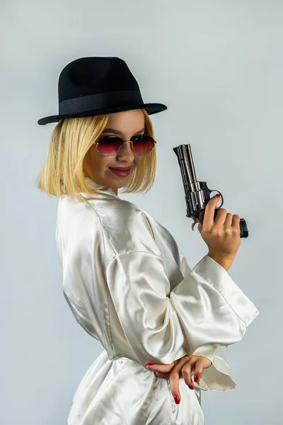 黒の帽子の中にポーズをとって銃を持っているドレッシングガウンにセクシーなエレガントな女性の肖像画 スタジオ撮影のコンセプト 単純な背景に隔離され — ストック写真