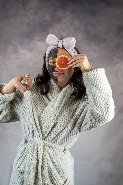 Mooi Meisje Witte Badjas Met Zwart Gezichtsmasker Die Grapefruit Geïsoleerd — Stockfoto
