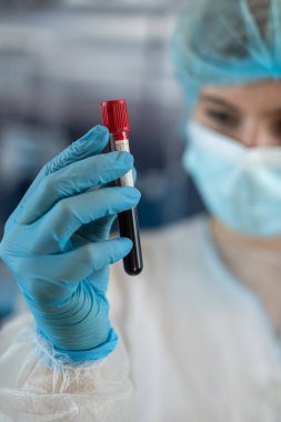 Koruyucu giysi tutan kadın bilim adamı klinik laboratuarında kan test tüplerini analiz ediyor. Kavram