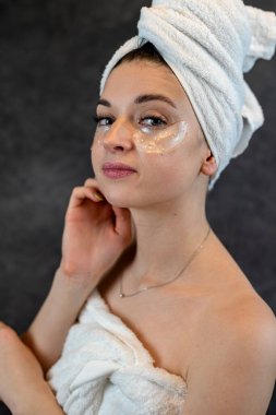 Çekici bir kadın, siyah üzerine izole edilmiş kameraya yapıştırılmış göz bantlı havlu giyer. Göz altındaki kırışıklıkları azaltmak için estetik prosedür