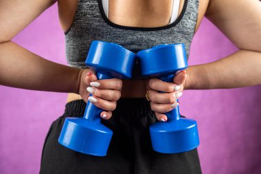 Genç, eğlenceli, güçlü spor spor antrenörü eşofmanlı kadın, arka planda izole haldeki halterleri tutuyor. Spor antrenmanı konsepti