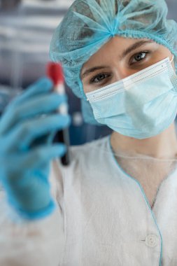 Koruyucu giysi tutan kadın bilim adamı klinik laboratuarında kan test tüplerini analiz ediyor. Kavram