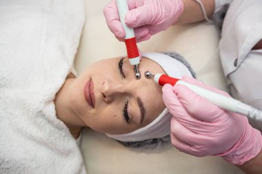 Genç ve güzel bir kadın güzellik kliniğinde mikro akım terapi görüyor. Elektrikli yüz tedavisi uyarıcısı 
