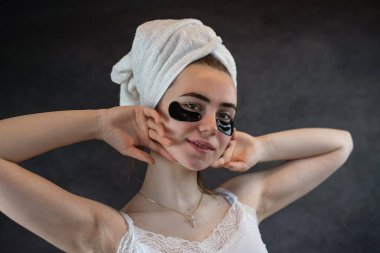 Büyüleyici genç bir kadın siyah göz altı bantlarıyla yaşlanma karşıtı prosedürler uyguluyor. Cilt bakımı kavramı