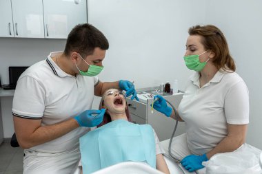 Gülümseyen dişçi ve bir asistan dişçi muayenehanesinde dişlerini kontrol ederken bir hastayla konuşuyor. dişçi dişleri