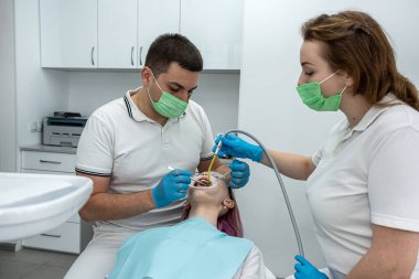 Erkek dişçi ve bayan asistan dişçi kliniğinde gülümseyen genç bir kadını ameliyat ediyorlar. Oral bakım kavramı