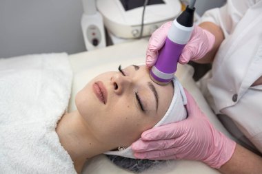 Yüzüne alet fonoforezi uygulayan genç bir kadın. Donanım yüz temizleme prosedürü. 