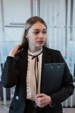 Beyaz kadın ofis müdürü. Ofiste görevli ve elinde pano var.. 