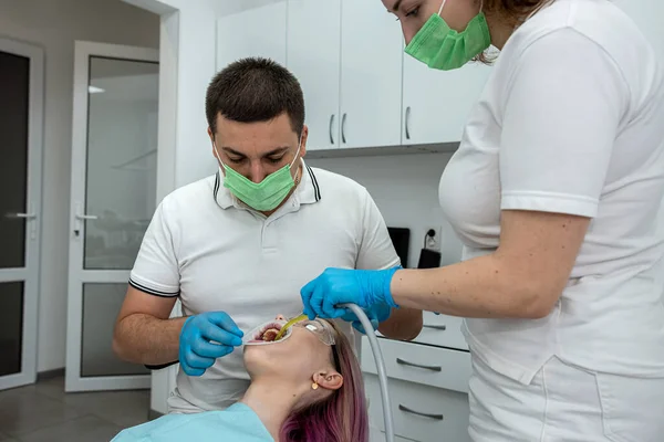 男性歯科医は歯科事務所の満足した女性顧客の助手と治療を行っています 人々は話し合い お互いを見ます — ストック写真