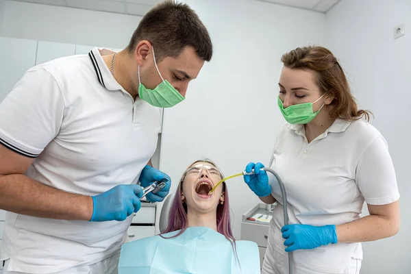 young woman has her teeth treated by a male dentist and a female assistant during an appointment at a dental clinic. dentistry teeth