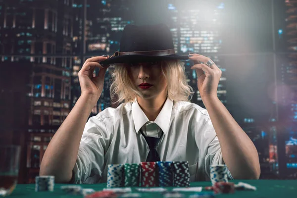 stock image Beautiful dealer girl in a hat in a shirt and tie at the poker table. follows the process. game. deception. machinations