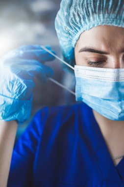 Klinikteki vardiyadan sonra tıbbi maskesini çıkartan yorgun genç doktorun portresi. Sağlık hizmetleri kavramı