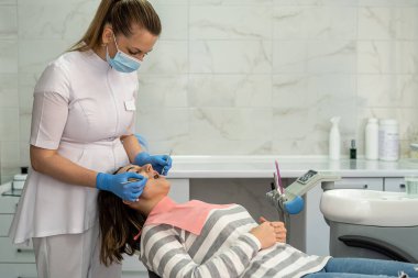 Dişçi, dişçi kliniğindeki kadın hastasını ayrıntılı bir şekilde muayene ediyor. Sağlık Hizmetleri