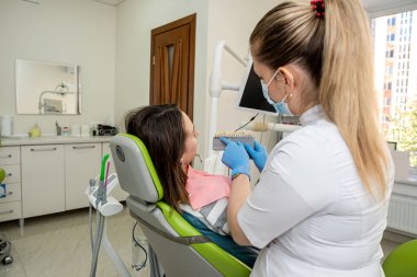 Stomatolog kadın hastaların beyazlatılması için diş örnekleri, implantların en iyi rengini seçmek için diş prosedürleri tutuyor. 