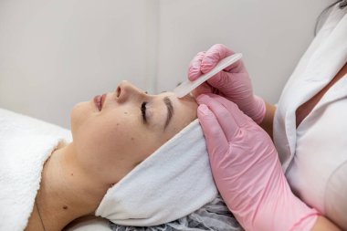 Kozmetik uzmanı müşterinin yüzüne beyaz guaj kazıyıcı sürerek tıbbi işlem yapıyor. Sağlık yaşam tarzı