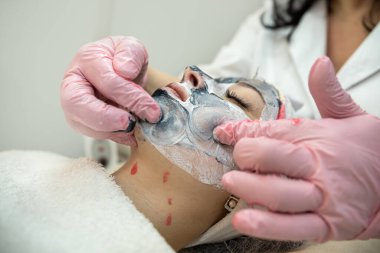 Kozmetik uzmanı müşterinin yüzüne bir maske taktı ve yüz kaldırma masajı yapıyor. Yenilenme işlemi ve cildin tazelenmesi
