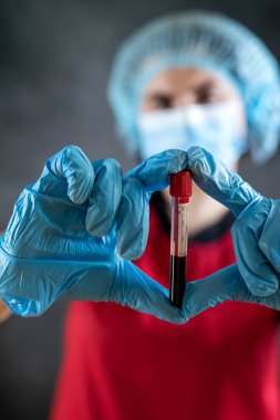Kırmızı üniformalı laboratuvar asistanı, siyah üzerinde izole edilmiş test tüpündeki kan örneklerine bakıyor. Covid19 pozitif test sonucu. Tıbbi tanı 
