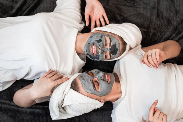 two beautiful sister lying on the floor with clay mask on face. Healthy skin and beauty concept. Skin care for all ages