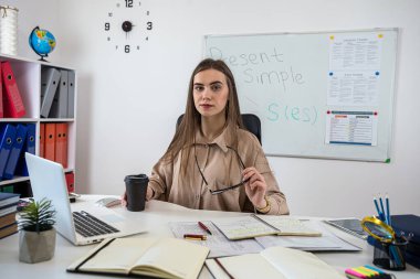 Genç bayan öğretmen masada oturmuş çevrimiçi ya da çevrimdışı İngilizce dersi veriyor. Konsept çalış