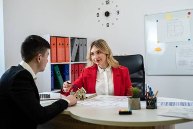 Ofiste yeni bir ev almak için kadın yönetici ile erkek müşteri toplantısı. Ev planı, plan ve dizüstü bilgisayar ofis masasında..